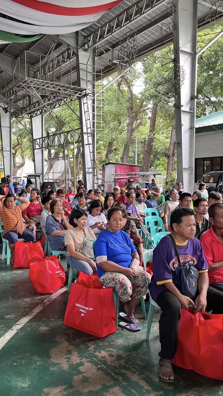 Rows of people seated on plastic chairs under the court's roof, red Muñozonian USA bags on the floor at their feet.