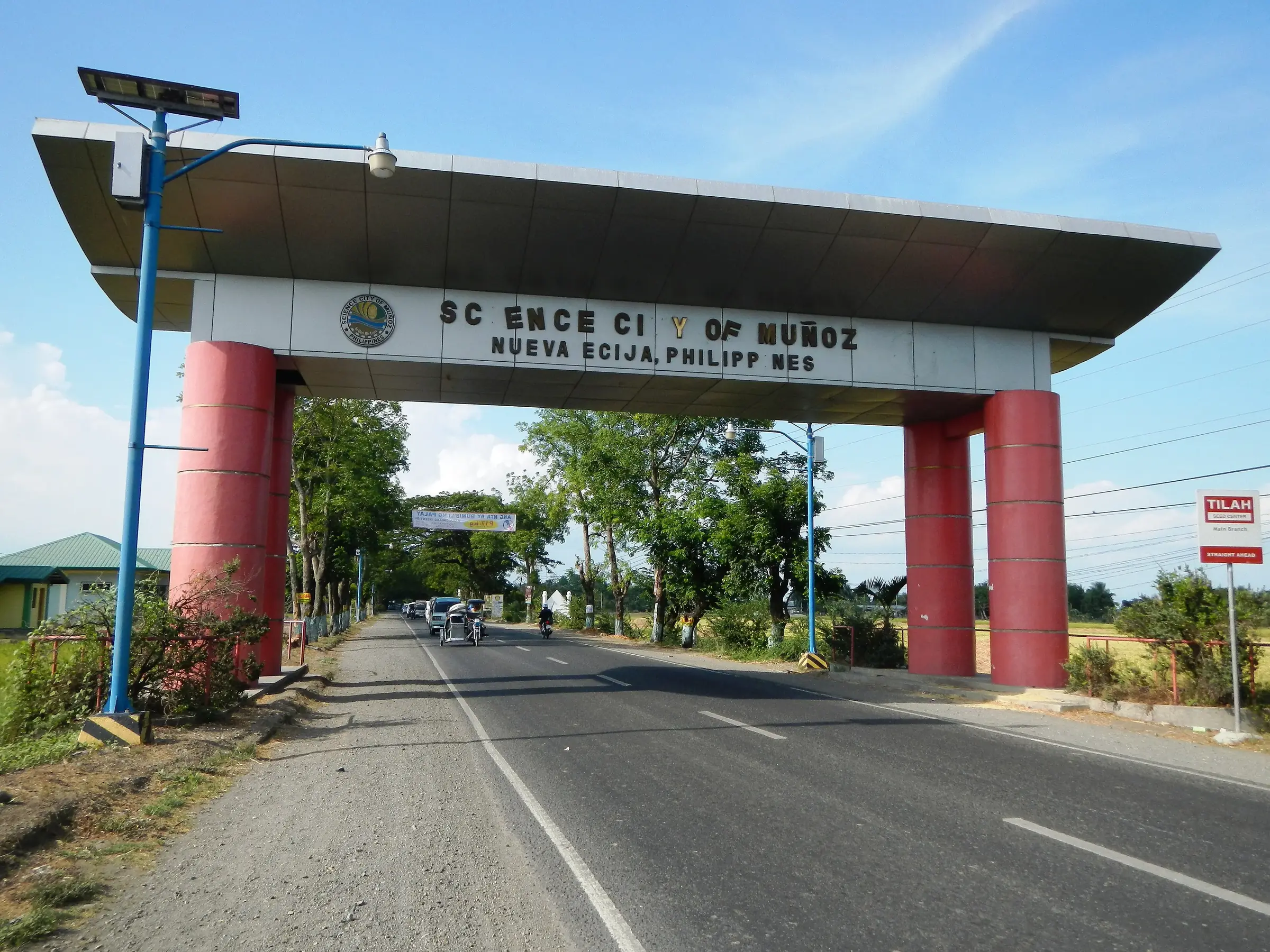 A road passing beneath the red-pillared welcome arch lettered Science City of Muñoz, Nueva Ecija, Philippines.